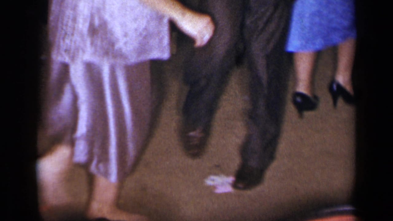 Adults' legs and feet moving on a dim indoor floor during a dance.