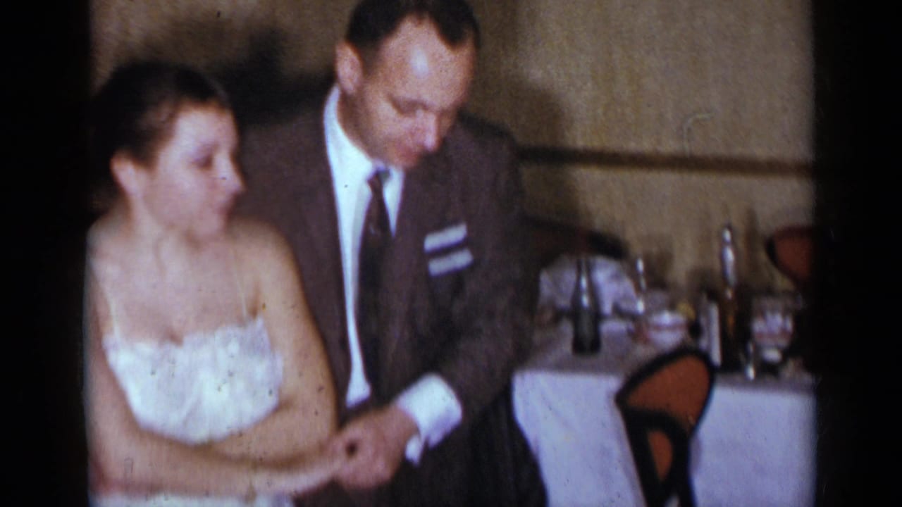 Young woman in a white dress and man in a suit sit close together at a dinner table.