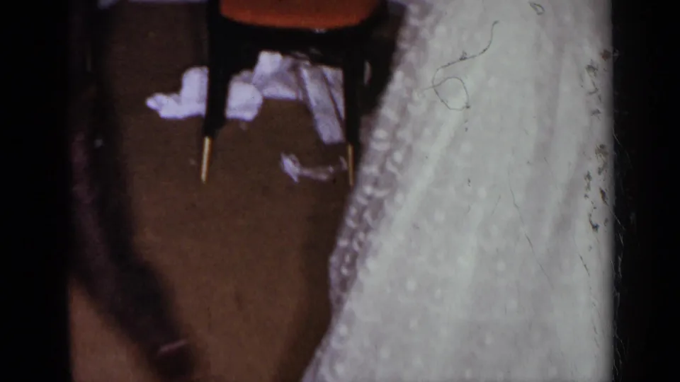The frame shifts to a close partial view of the woman's white dress, with a dining chair and floor visible nearby.