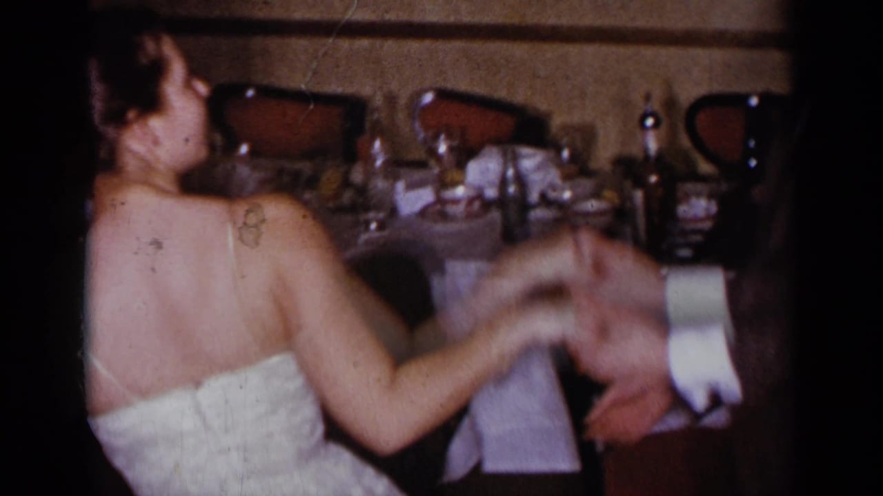Woman in a white strapless dress dances beside a set table while holding a man's hand.