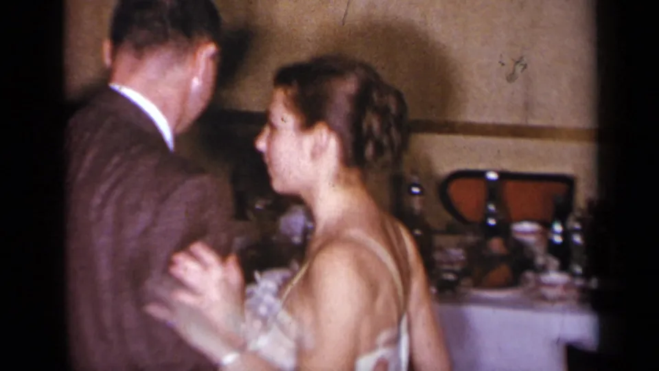 A woman in a white dress and a man in a brown suit dance together in the supplied 1954 New York home-movie clip.