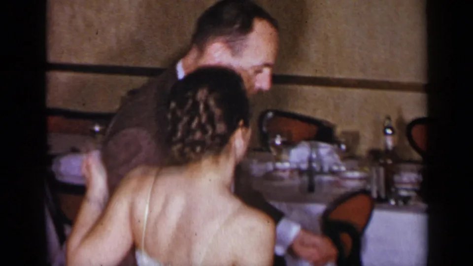 The couple continues dancing in a dim private interior, with the woman's braided updo and the man's brown suit visible.