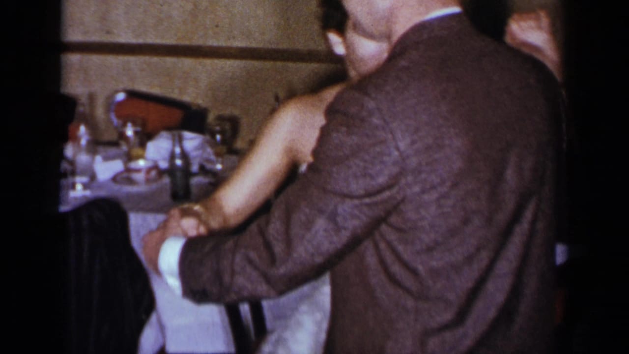 Couple dancing closely beside banquet tables in a dim indoor room.