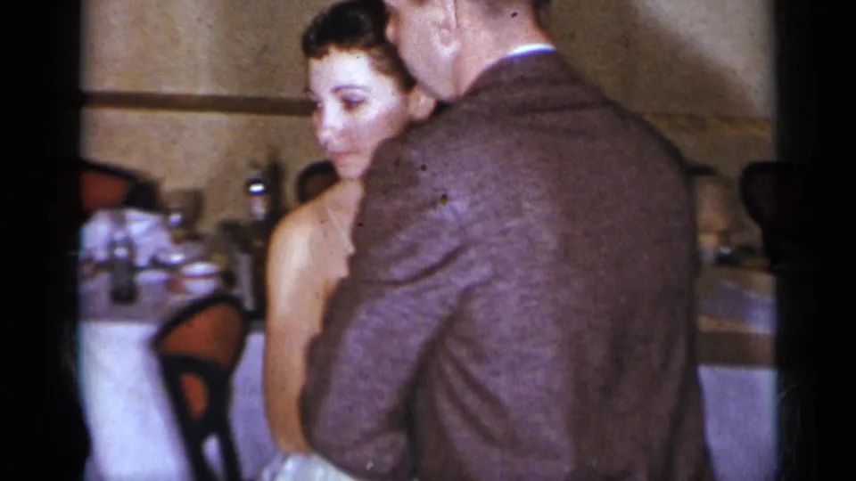 1954 New York home-movie frame showing a woman in a white dress and a man in a brown jacket dancing in a formal dining room.