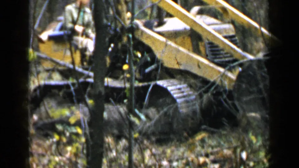 A male operator is visible on a yellow tracked compact construction vehicle in a wooded Birmingham-area setting, filmed on 8mm in 1957.