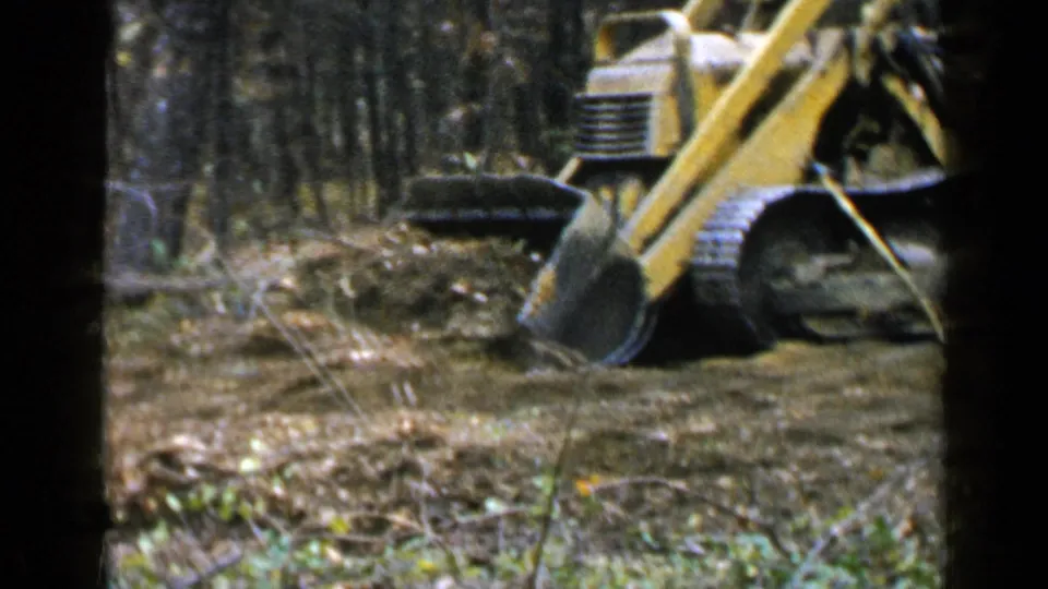 The bulldozer’s bucket is lowered into disturbed soil among trees in the Birmingham-area 8mm footage.