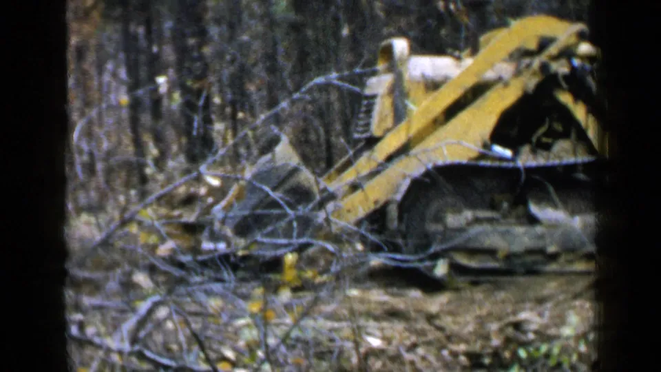 The 1957 Birmingham land-clearing footage shows the tracked bulldozer behind foreground branches in dense woods.