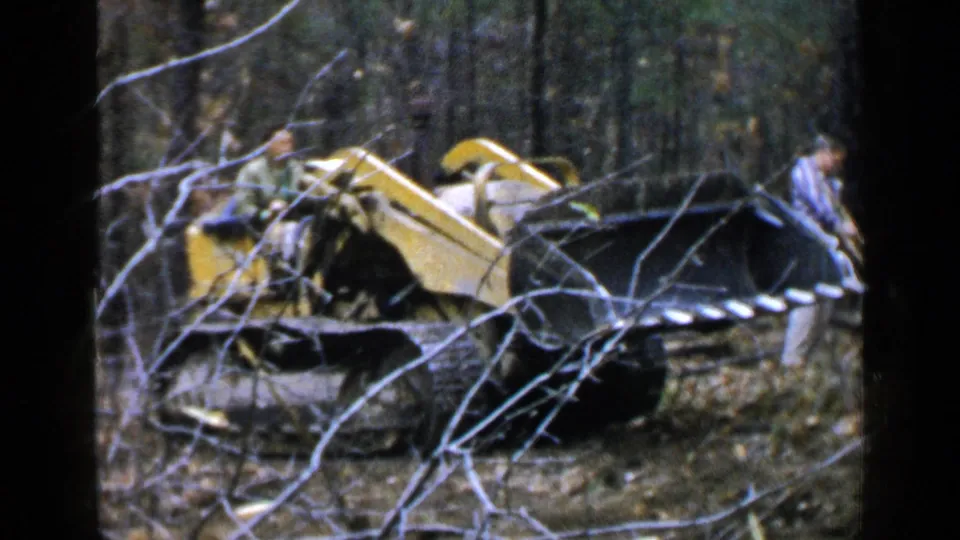 The Birmingham 1957 clip ends with the bulldozer framed by branches, the operator aboard, and another adult partly visible nearby.