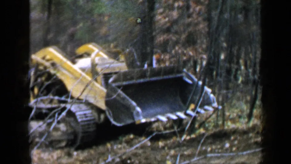The yellow loader advances along a wooded path, its large black bucket facing the camera in the Birmingham home-movie frame.