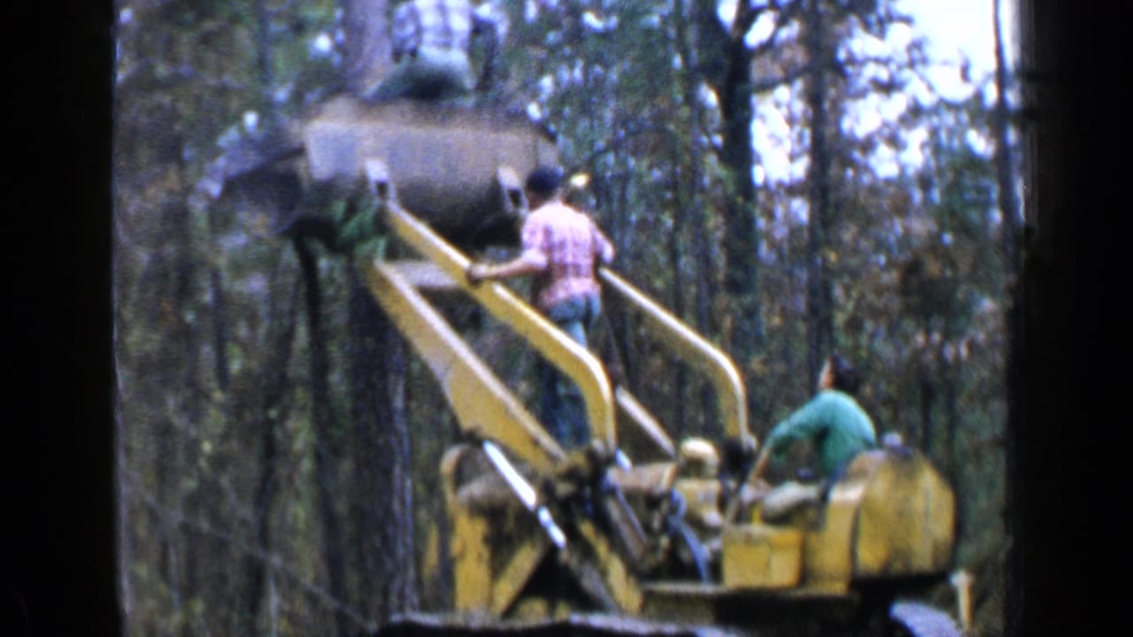 Birmingham, Alabama 1957 footage showing men around a yellow elevated logging machine in a wooded area.