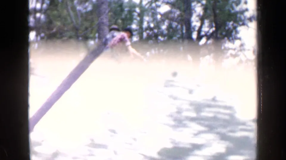 Bright 8mm frame from the 1957 Birmingham clip showing a worker partly obscured by exposure and a long timber or machine element.