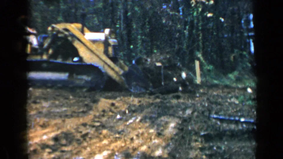 In 1957 Birmingham-area footage, a yellow tracked bulldozer works through brush and exposed dirt in a wooded clearing.