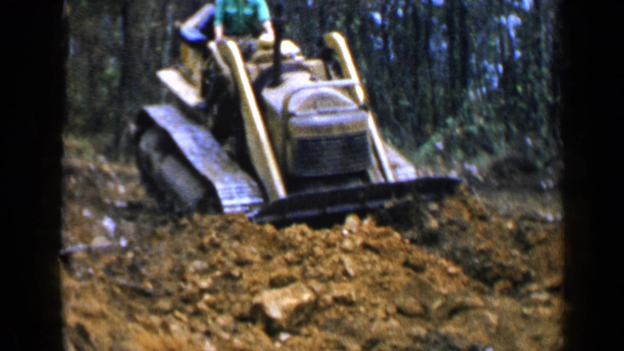 Yellow bulldozer pushing a dirt pile in a wooded area.