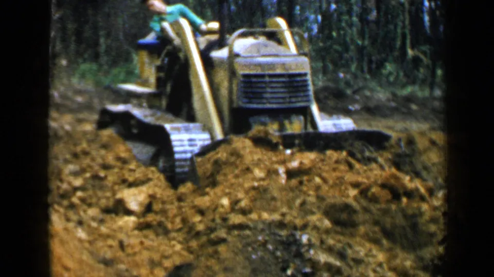 A yellow crawler bulldozer faces the camera while clearing rocky soil in a wooded Birmingham, Alabama scene from 1957.