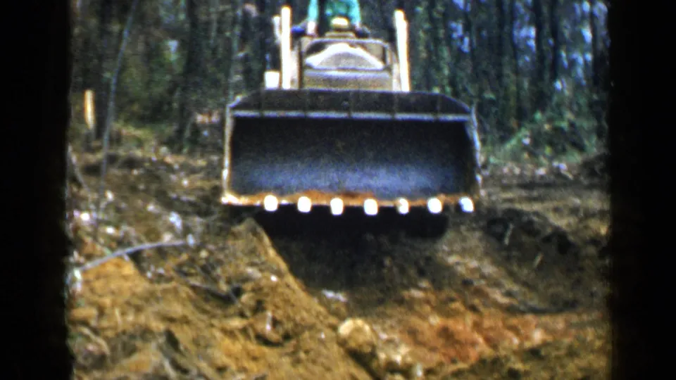 Yellow tracked bulldozer faces the camera in wooded Birmingham-area terrain, with its blade low against the ground.