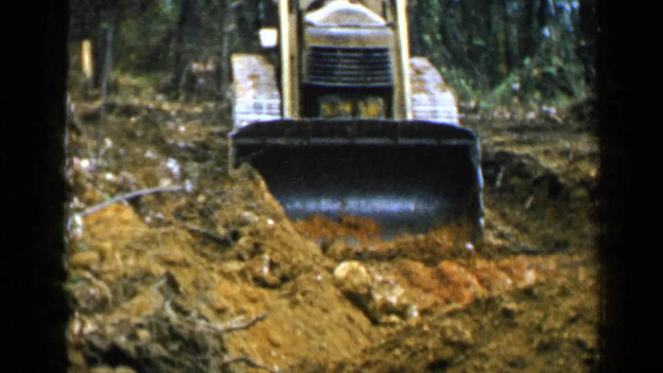 Close front view of the yellow bulldozer and blade moving over uneven soil in 1957 Birmingham-area home-movie footage.