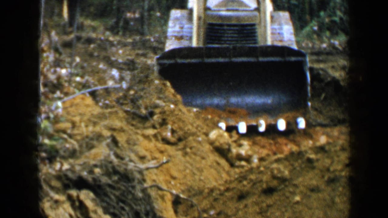1957 Birmingham-area 8mm frame showing a tracked bulldozer or loader pushing earth near trees.