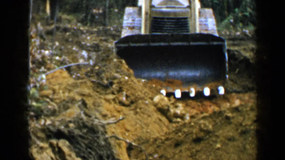 1957 Birmingham-area 8mm frame showing a tracked bulldozer or loader pushing earth near trees.