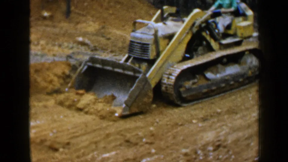 1957 Birmingham, Alabama frame showing the loader bucket low to the ground as it moves earth beside trees.