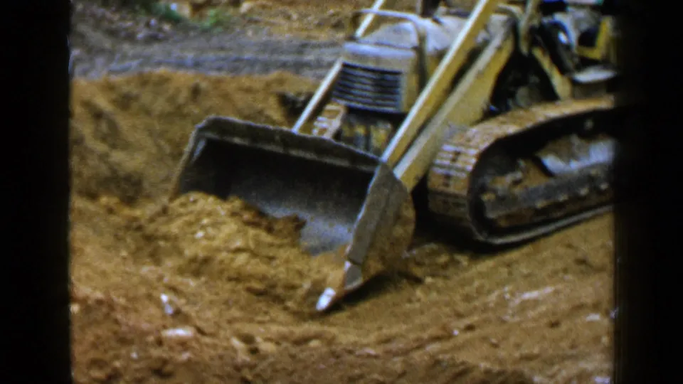 Home-movie still from Birmingham in 1957 showing a yellow tracked loader close to the camera while clearing sand.