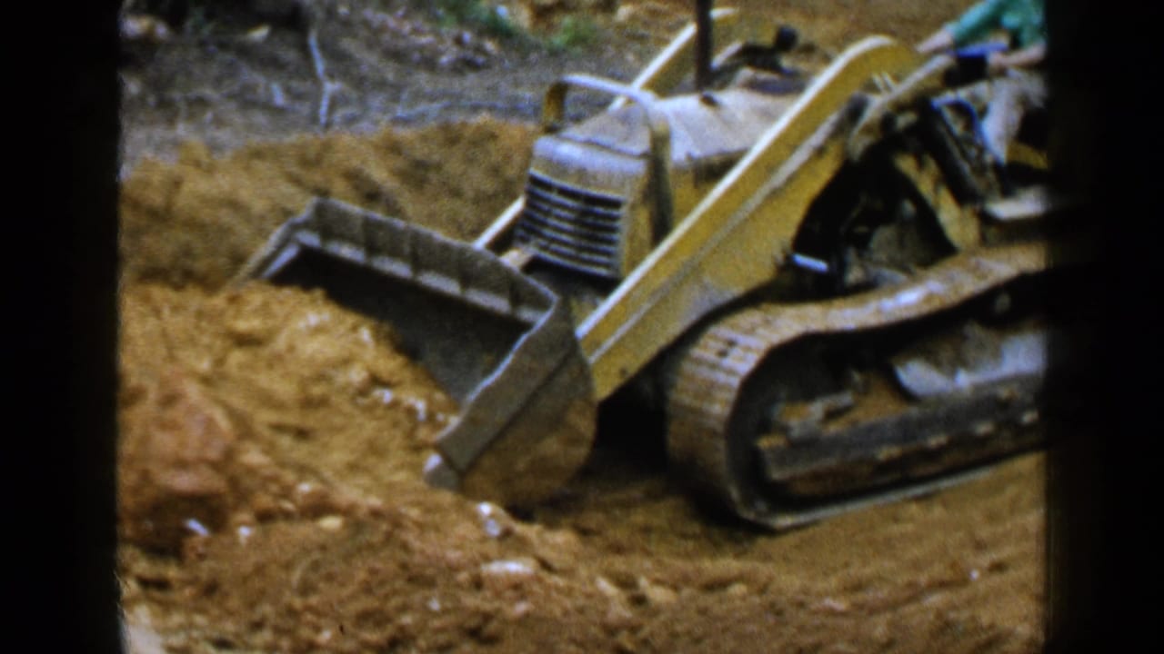 Yellow tracked front-end loader pushes into a mound of loose dirt at a construction site.