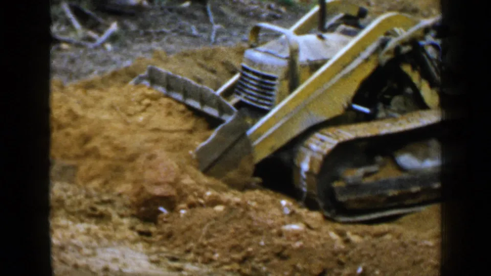 The loader appears in profile with its scoop near the dirt pile, framed by rough ground and 8mm film borders.