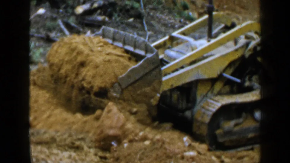 The loader gathers a rounded heap of soil in front of its scoop, showing active earthmoving in the Birmingham construction footage.