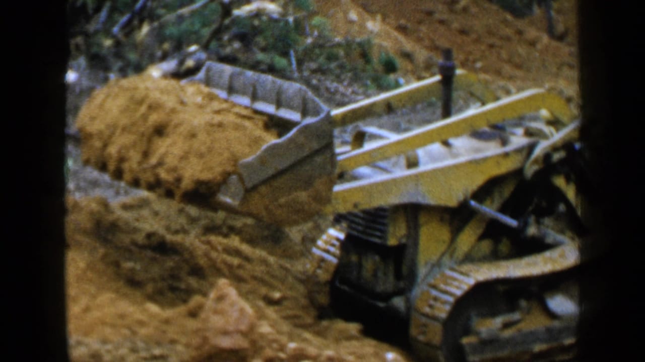 Yellow tracked bulldozer pushing a mound of dirt in a wooded area.