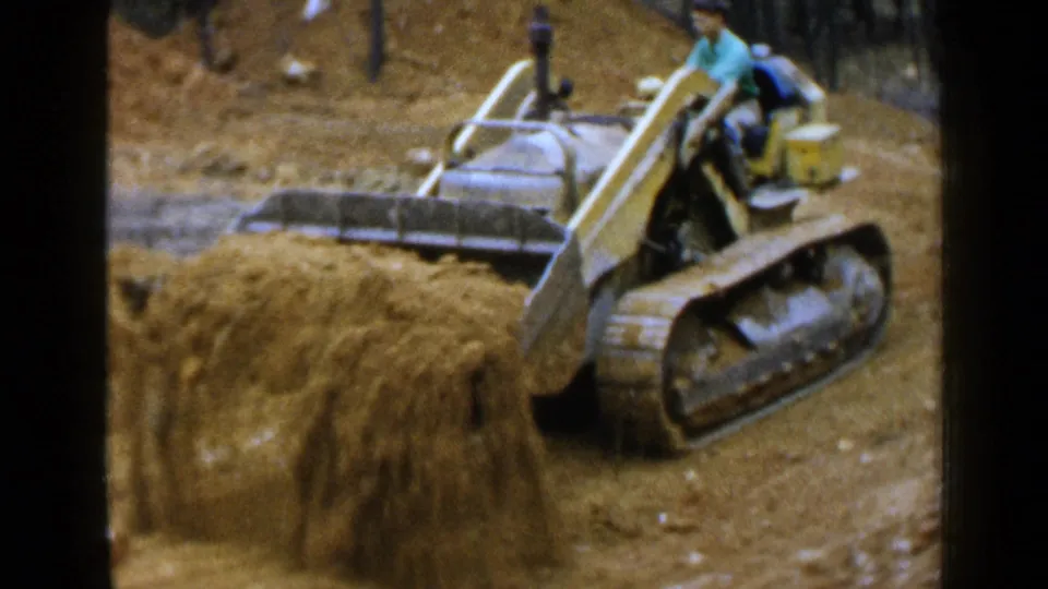 1957 Birmingham home-movie view of a yellow tracked bulldozer beside a high mound of earth, with the operator seated at the controls.