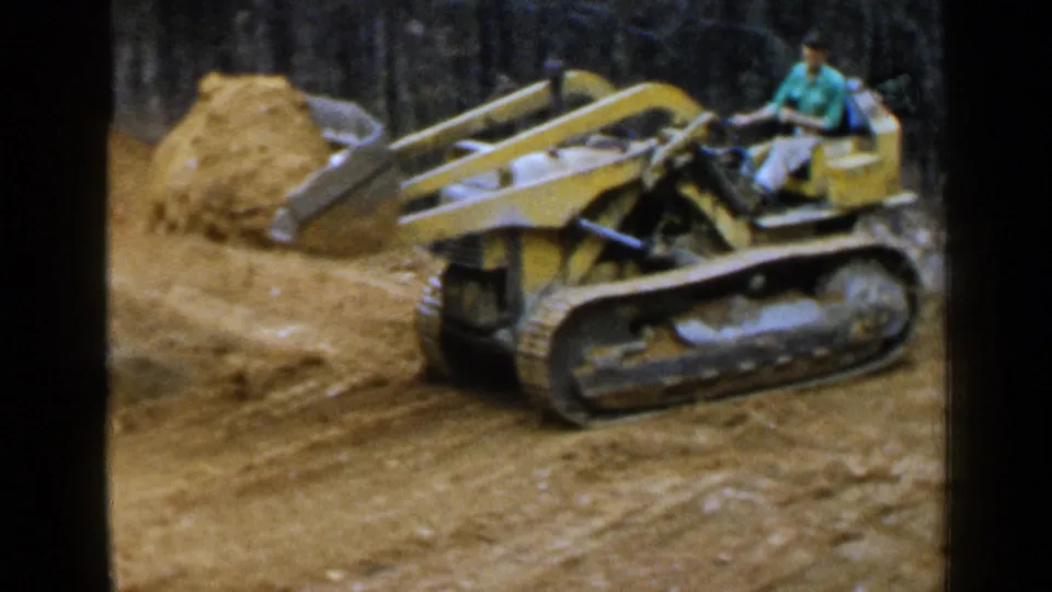 Yellow tracked earthmoving machine operated by a man at a wooded Birmingham worksite in 1957.