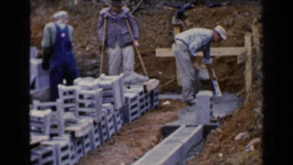 In Birmingham, Alabama in 1957, workers handle concrete blocks and cement beside wooden bracing in a muddy excavation.
