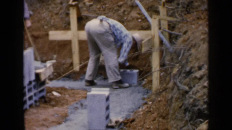 A 1957 Birmingham construction view shows a worker reaching down to set or adjust a cinder block along a concrete foundation line.