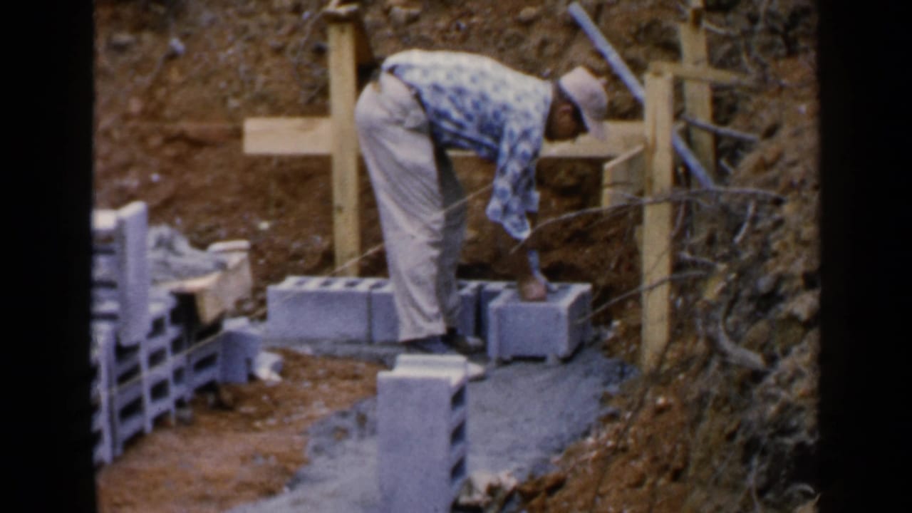 Man bends over a row of grey concrete blocks at a dirt construction site.
