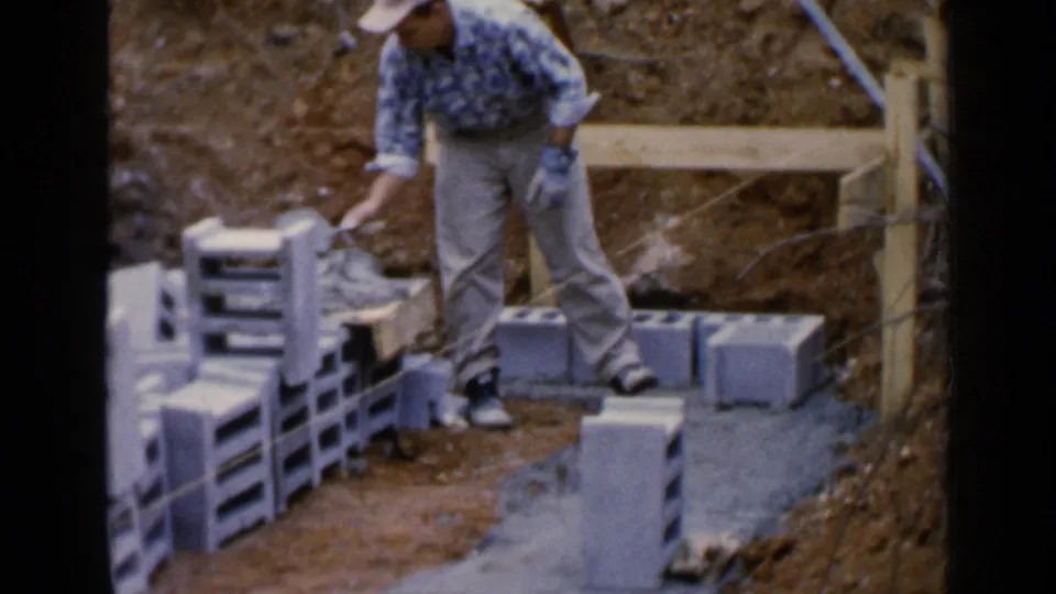 A man in a patterned shirt and tan pants works beside concrete blocks and timber supports in Birmingham, Alabama, 1957.