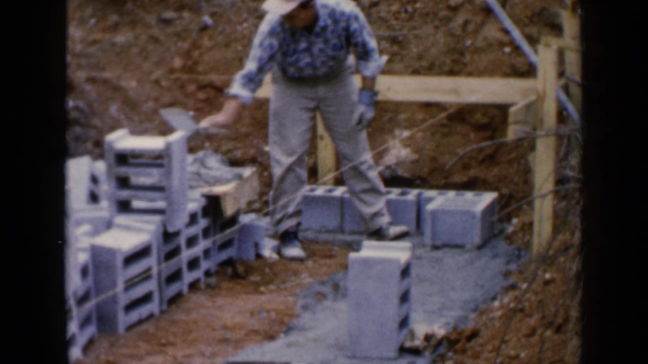 Man standing beside cinder blocks at a dirt construction site.