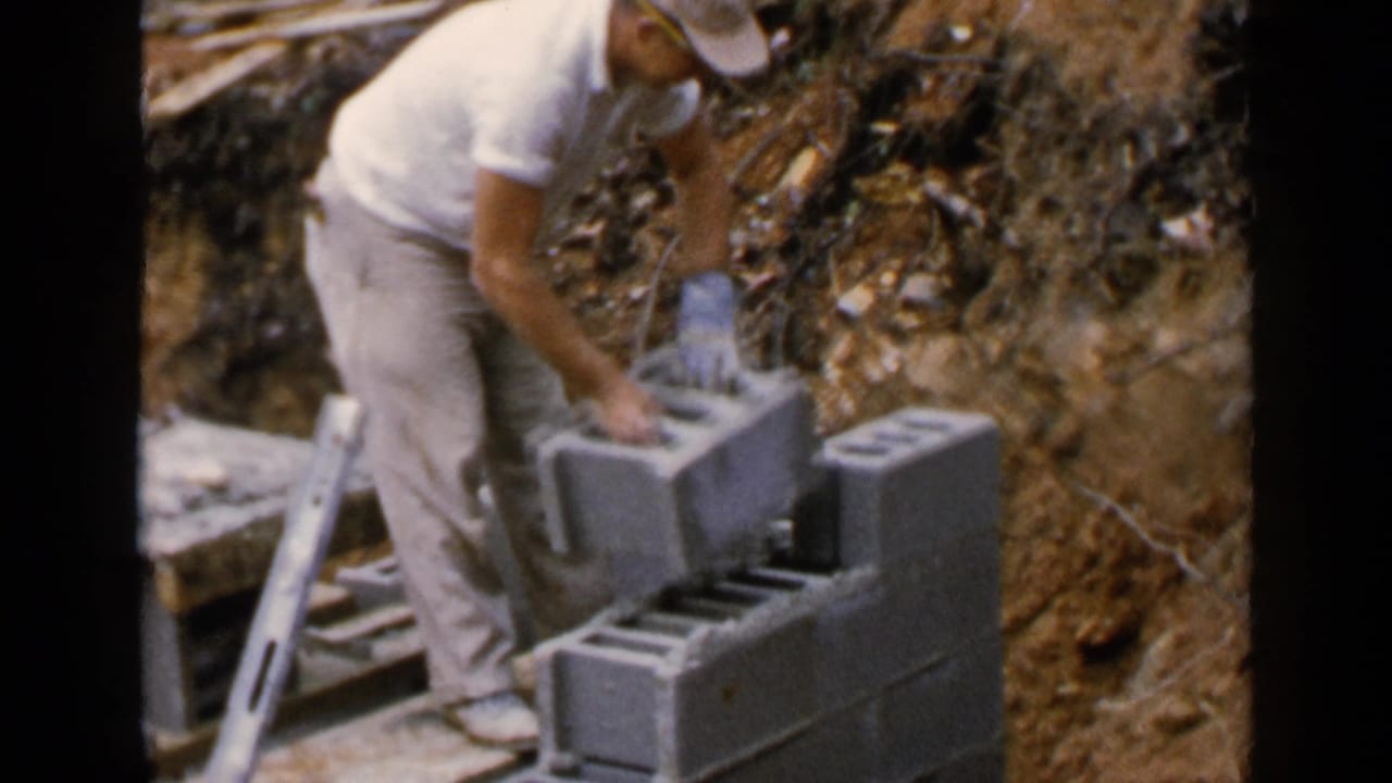 Man positions a concrete block on a low wall beside exposed earth.