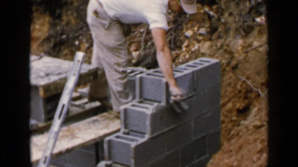 The worker appears to place or adjust a cinder block on a low wall at the Birmingham construction site.