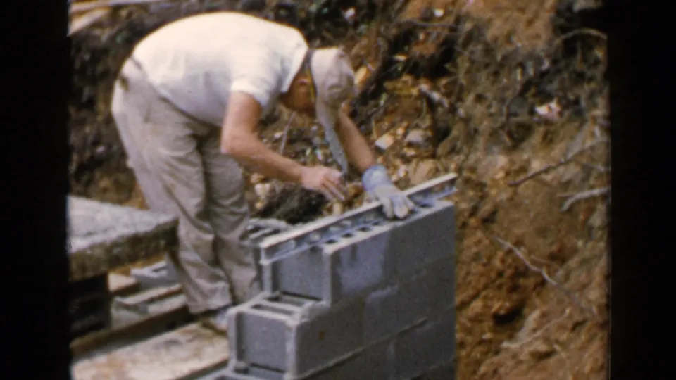 Worker in a white shirt and cap checks alignment on concrete blocks at the Birmingham construction site.