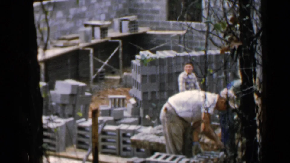 Worker bends near a block wall as other people stand in the background of the Birmingham construction scene.