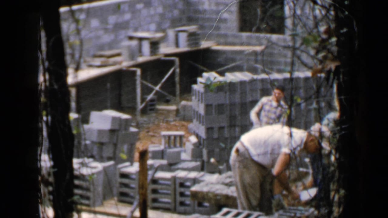 Workers among cinder blocks and timber supports at a partially built structure.