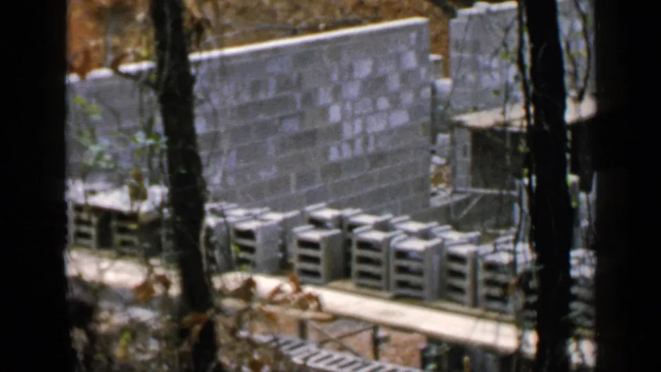 Cinder block structure under construction in Birmingham, framed by trees with stacks of blocks and simple wooden supports nearby.