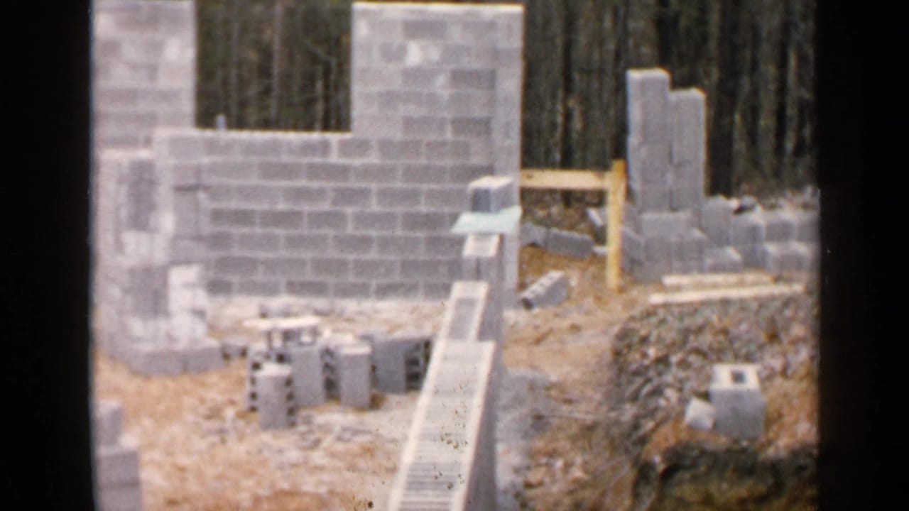 Concrete block walls and loose blocks on a dirt construction site near trees.