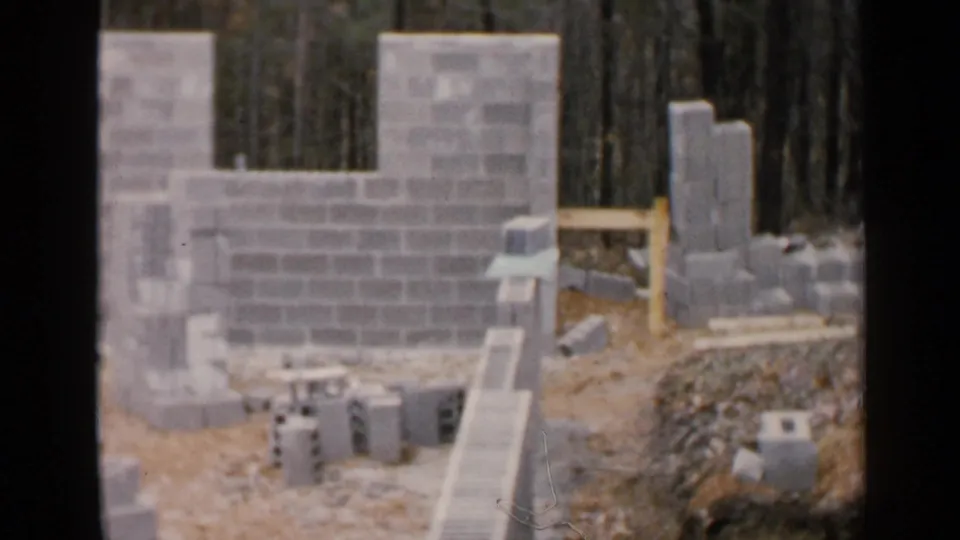 The frame shows a partially built concrete block structure in Birmingham, with loose blocks, lumber, and woods behind the site.