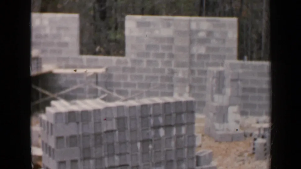 Stacks of concrete blocks fill the foreground while unfinished block walls and wood bracing appear behind them at the 1957 Birmingham site.