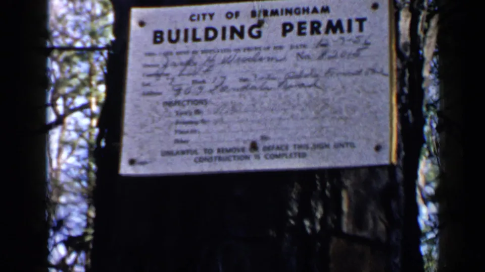 1957 Birmingham, Alabama footage showing a City of Birmingham building permit sign mounted on a tree among trunks and filtered daylight.