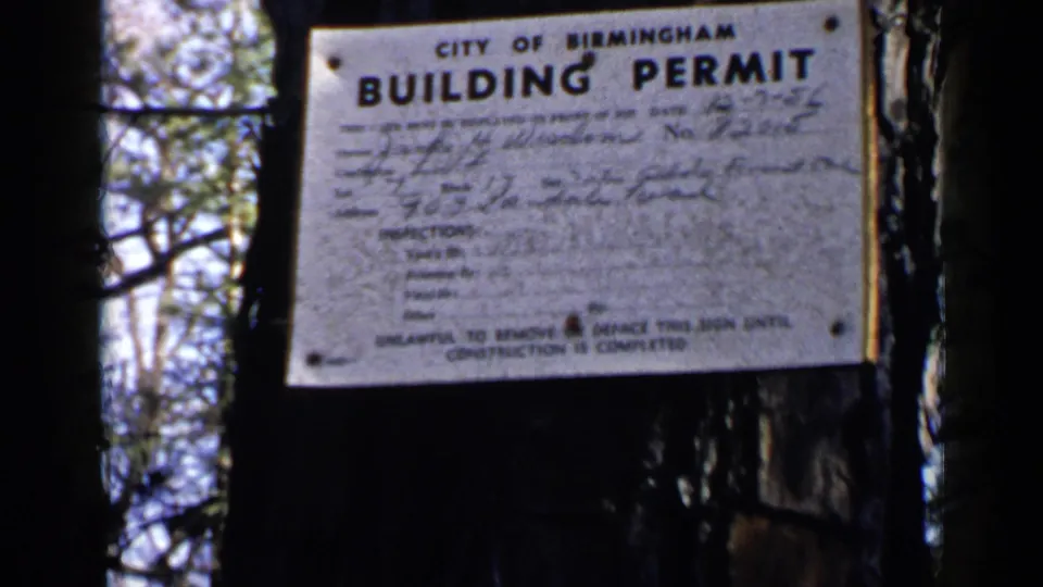 Close 1957 Birmingham view of the building permit sign, with official printed text and handwritten details partly legible on the metal surface.