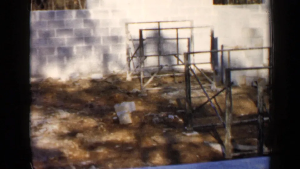 1957 Birmingham construction site with metal scaffolding, cinder block walls, and loose material on dirt ground.