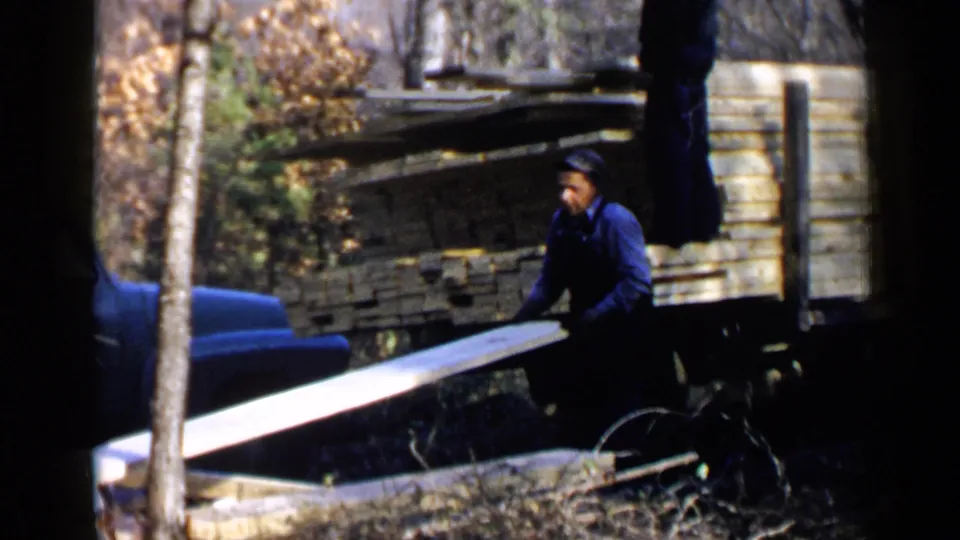 A worker in blue clothing unloads a long plank from a wooden truck bed in the Birmingham, Alabama 1957 clip.