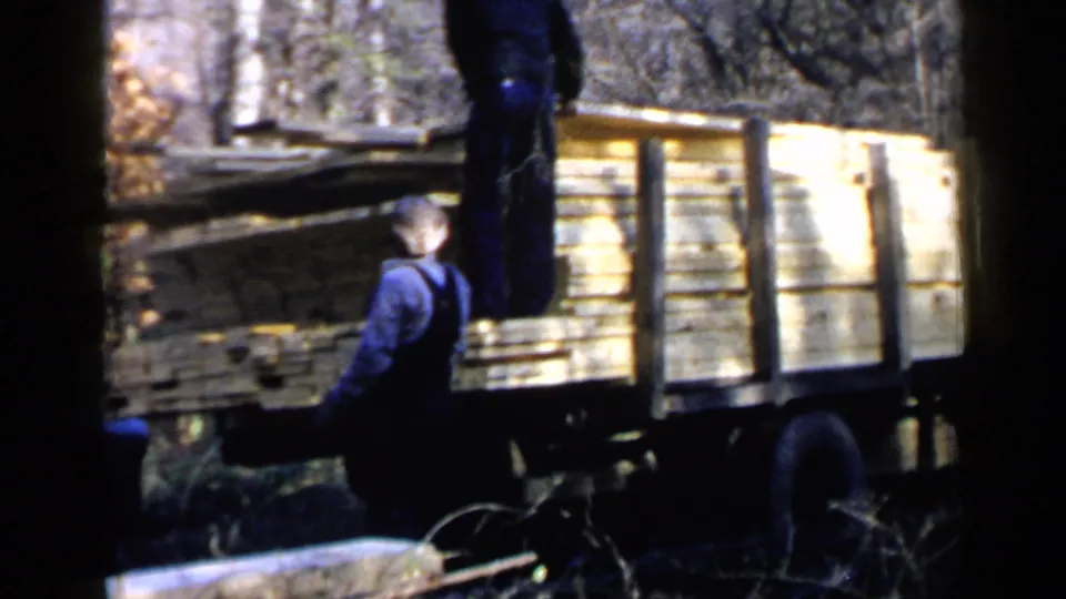 A man in blue overalls stands near the wooden-sided lumber truck in the Birmingham, Alabama 1957 home-movie scene.