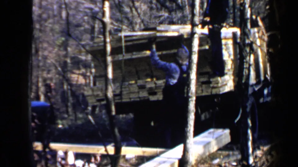 A man stands near the rear of a lumber truck in the Birmingham 1957 home-movie footage, with planks and trees visible.